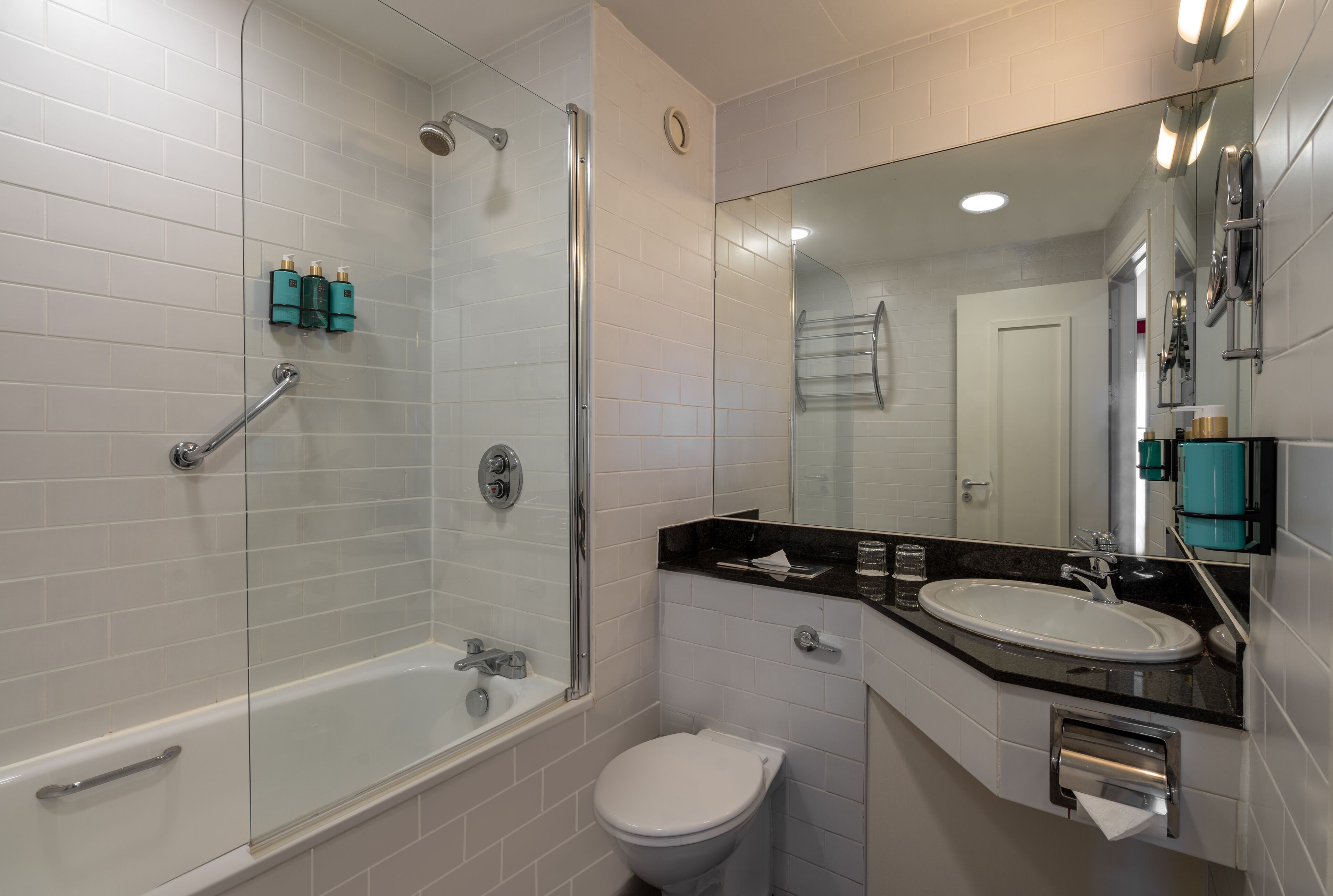 Een moderne badkamer met een douchecabine van glas, een wit toilet en een wastafel met een zwart aanrecht.