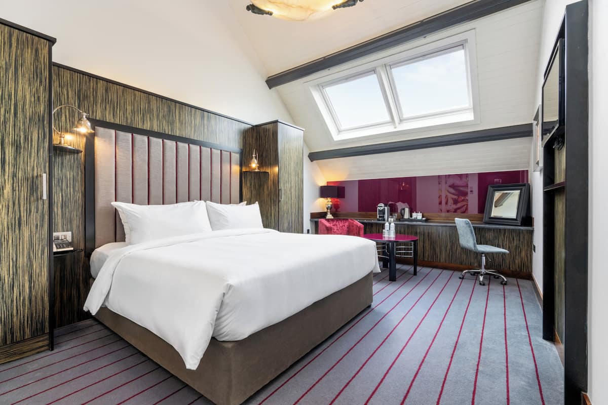 Hotellihuoneessa on suuri sänky, työpöytä ja tuoli. Siinä on myös ikkuna ja kattovalokuvio.