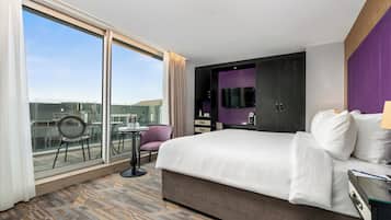 A hotel room with a large bed, a TV, a desk, and a view of the city.