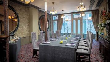 A formal dining room with a long table set for a meal, surrounded by high-backed chairs, and adorned with elegant chandeliers and a large mirror.