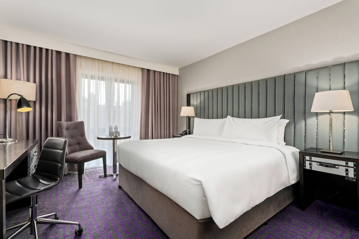 Hotellihuone, jossa on suuri sänky, työpöytä tuolilla, pieni pöytä ja kaksi lamppua.