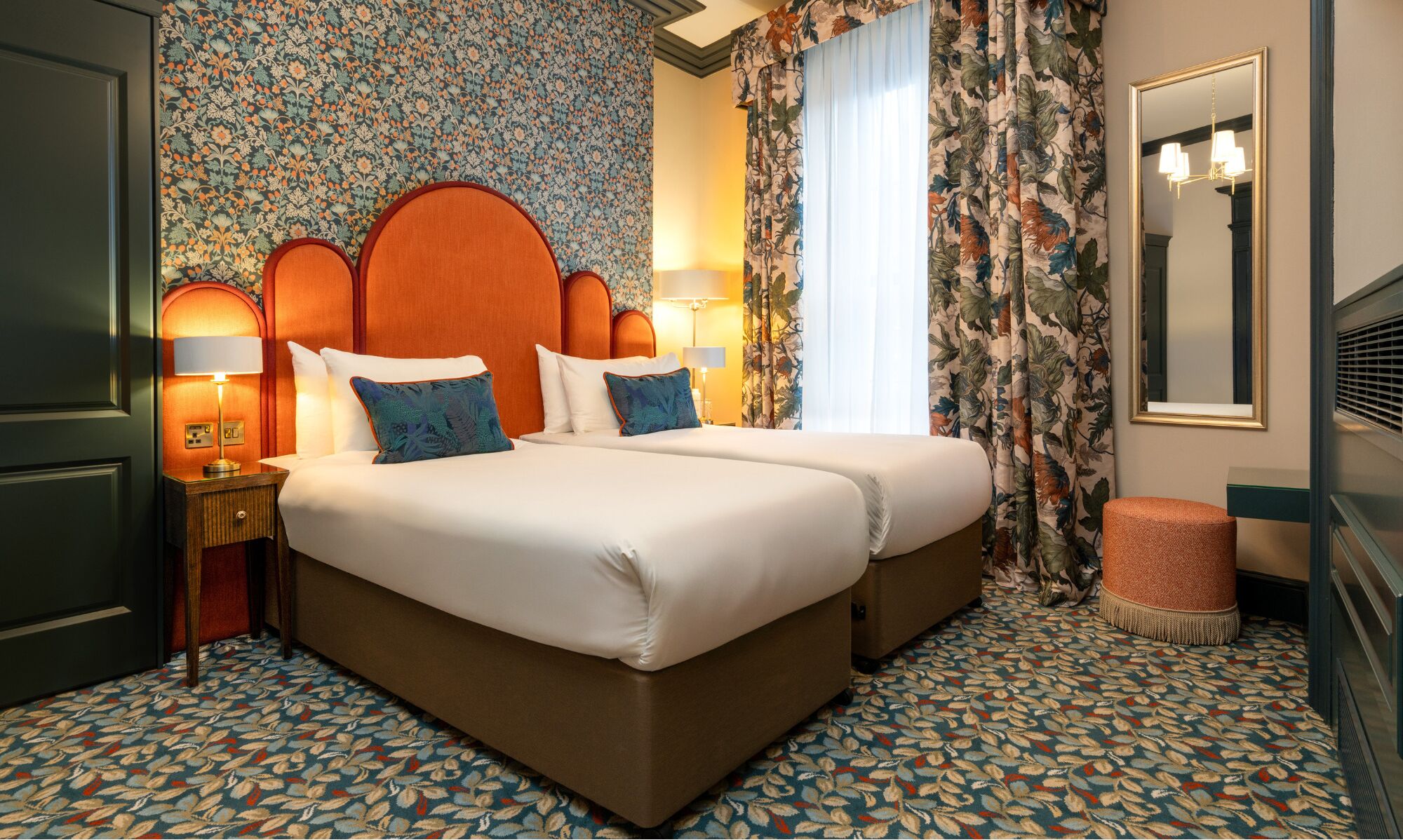 A double bed with a wooden headboard, two bedside lamps, and floral-patterned curtains.