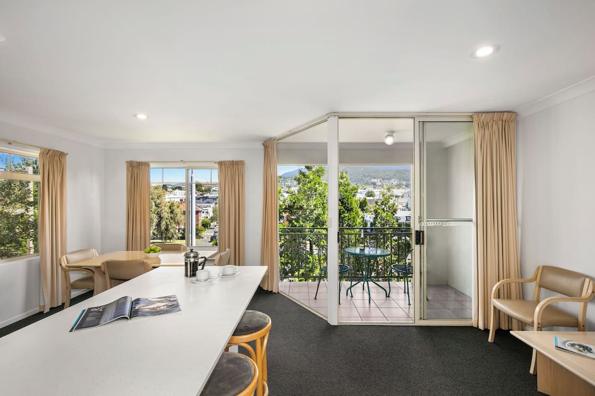 Une chambre d’hôtel moderne avec balcon, coin repas et vue sur la ville.