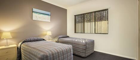 A hotel room with two beds, a nightstand with a lamp, a window with blinds, and a painting on the wall.