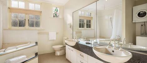 A bathroom with two sinks, a toilet, a window with frosted glass, and a large mirror.