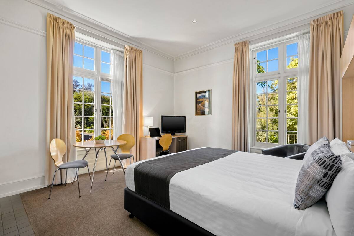 Une chambre d’hôtel avec un grand lit, un bureau avec un ordinateur portable, une télévision et deux chaises.