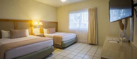 Una habitación de hotel con dos camas, un escritorio, un espejo y un ventilador de techo.