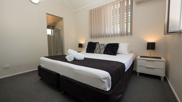 A hotel room with a large bed, a bedside table with a lamp, a wardrobe, and a mirror. - Marlin Cove Resort (Trinity Beach)