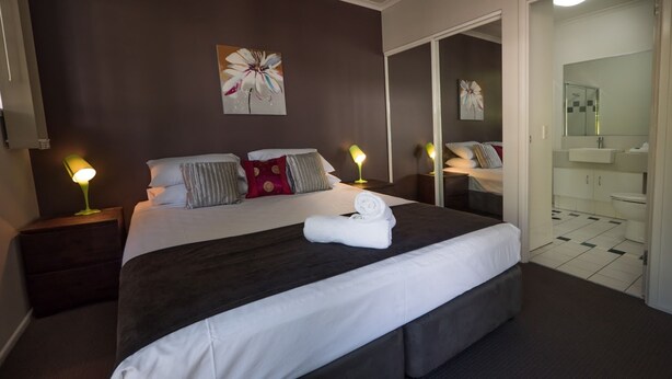 A neatly made bed with white linens, two bedside lamps, and a rolled towel on the bed. - Marlin Cove Resort (Trinity Beach)