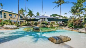 A resort pool with clear water, surrounded by rocks and palm trees, with a building in the background. - Marlin Cove Resort (Trinity Beach)
