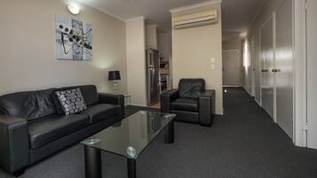 Ein modernes Wohnzimmer mit einem schwarzen Ledersofa, einem Glastisch, einem schwarzen Sessel und einem Gemälde an der Wand.
