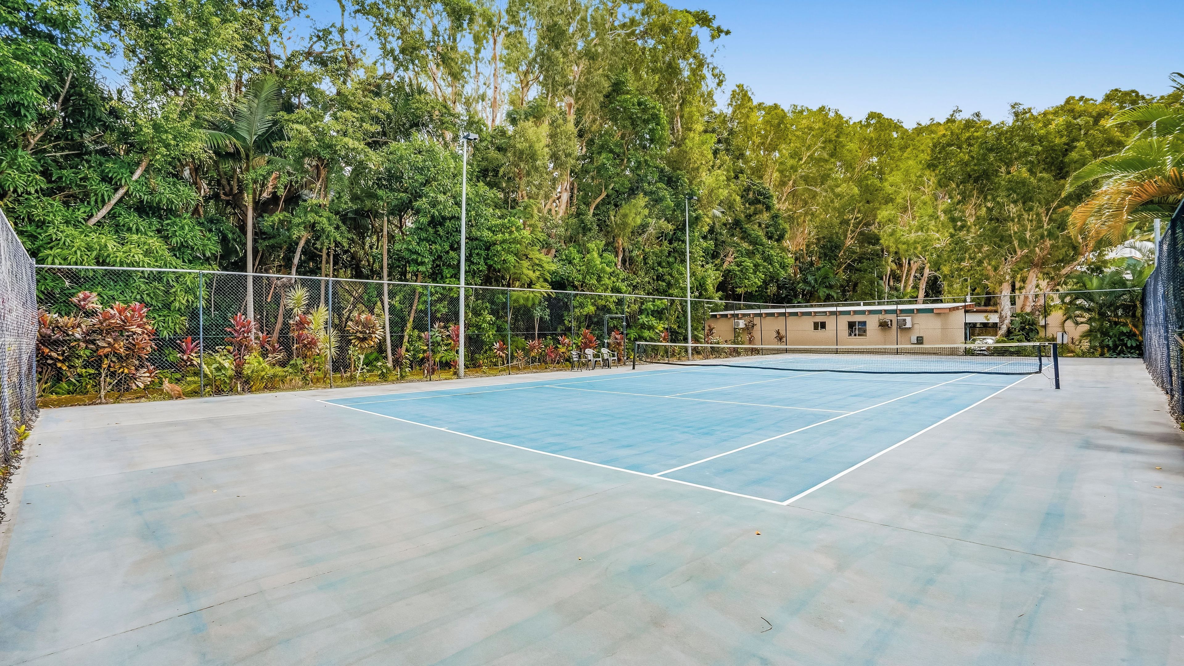 An outdoor tennis court surrounded by a fence and lush greenery.
