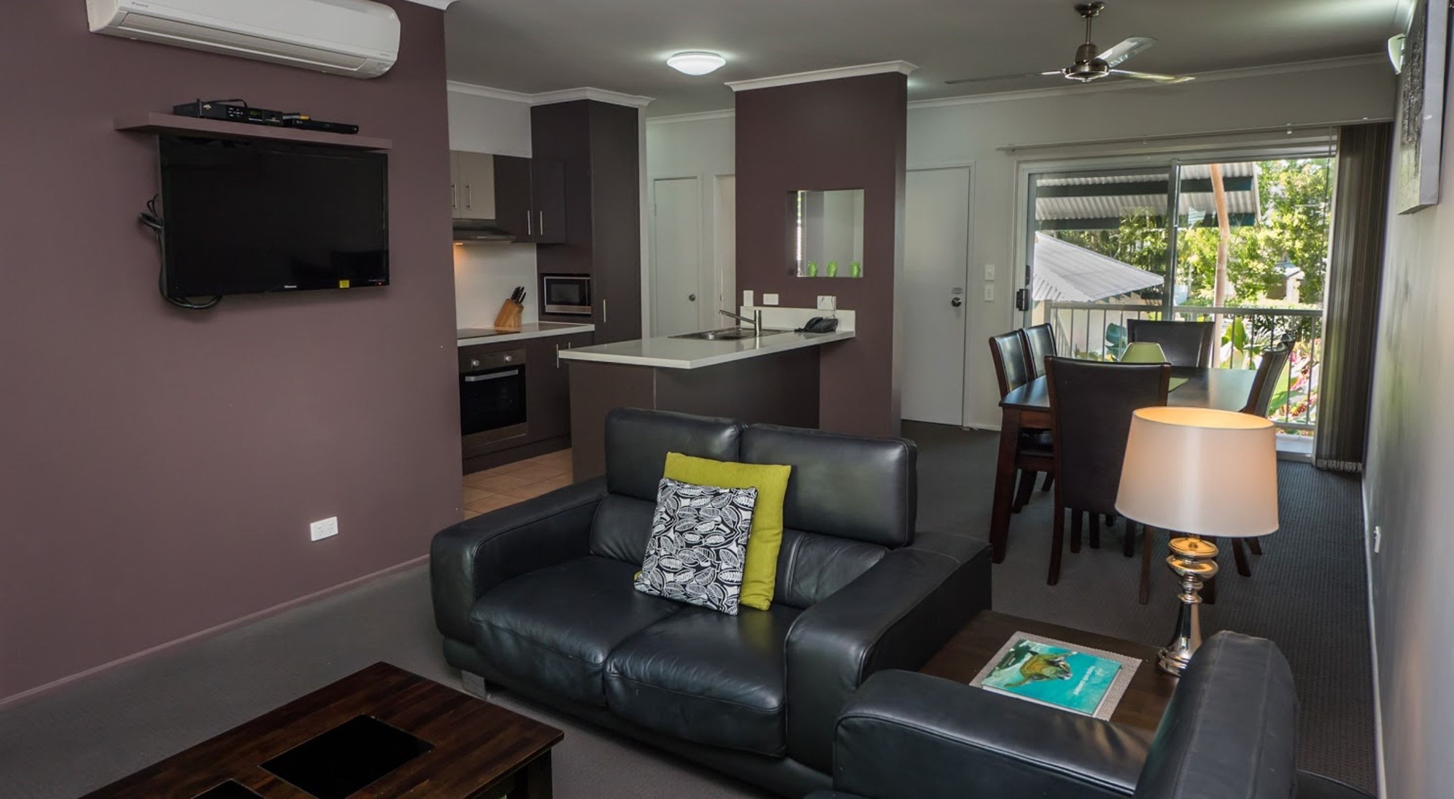 A modern living room with a black leather sofa, a small coffee table, and a dining area with a table and chairs.