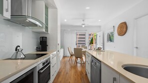 A modern kitchen with a kettle, coffee maker, and a dining area with chairs and a table. - Marlin Cove Resort (Trinity Beach)