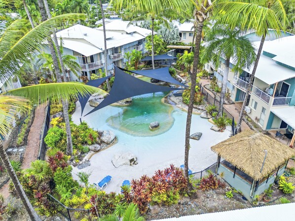 Un resort con piscina, palmeras y un edificio de techo de paja.