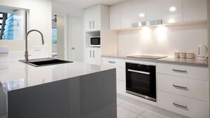 A modern kitchen with white cabinetry, a stainless steel sink, a microwave, and an oven. - Marlin Cove Resort (Trinity Beach)