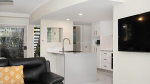 A modern kitchen with white cabinets, a central island, and a built-in microwave. - Marlin Cove Resort (Trinity Beach)
