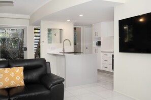 A modern kitchen with white cabinets, a central island, and a built-in microwave. - Marlin Cove Resort (Trinity Beach)