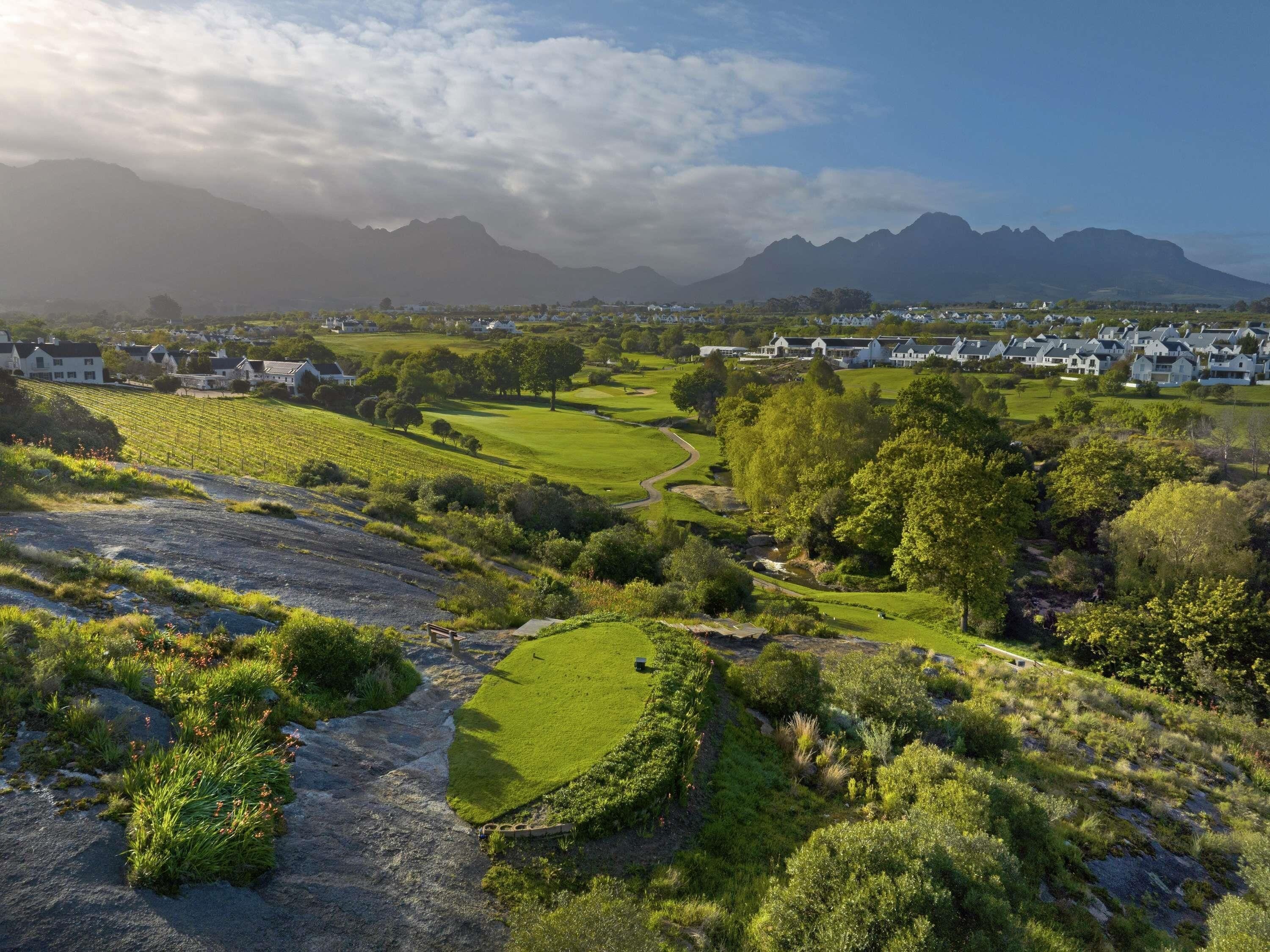 A rural landscape with houses, a golf course, and mountains in the background.