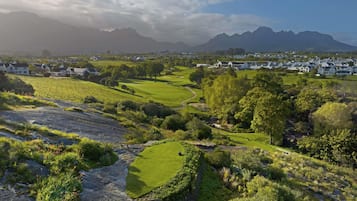 A rural landscape with houses, a golf course, and mountains in the background.