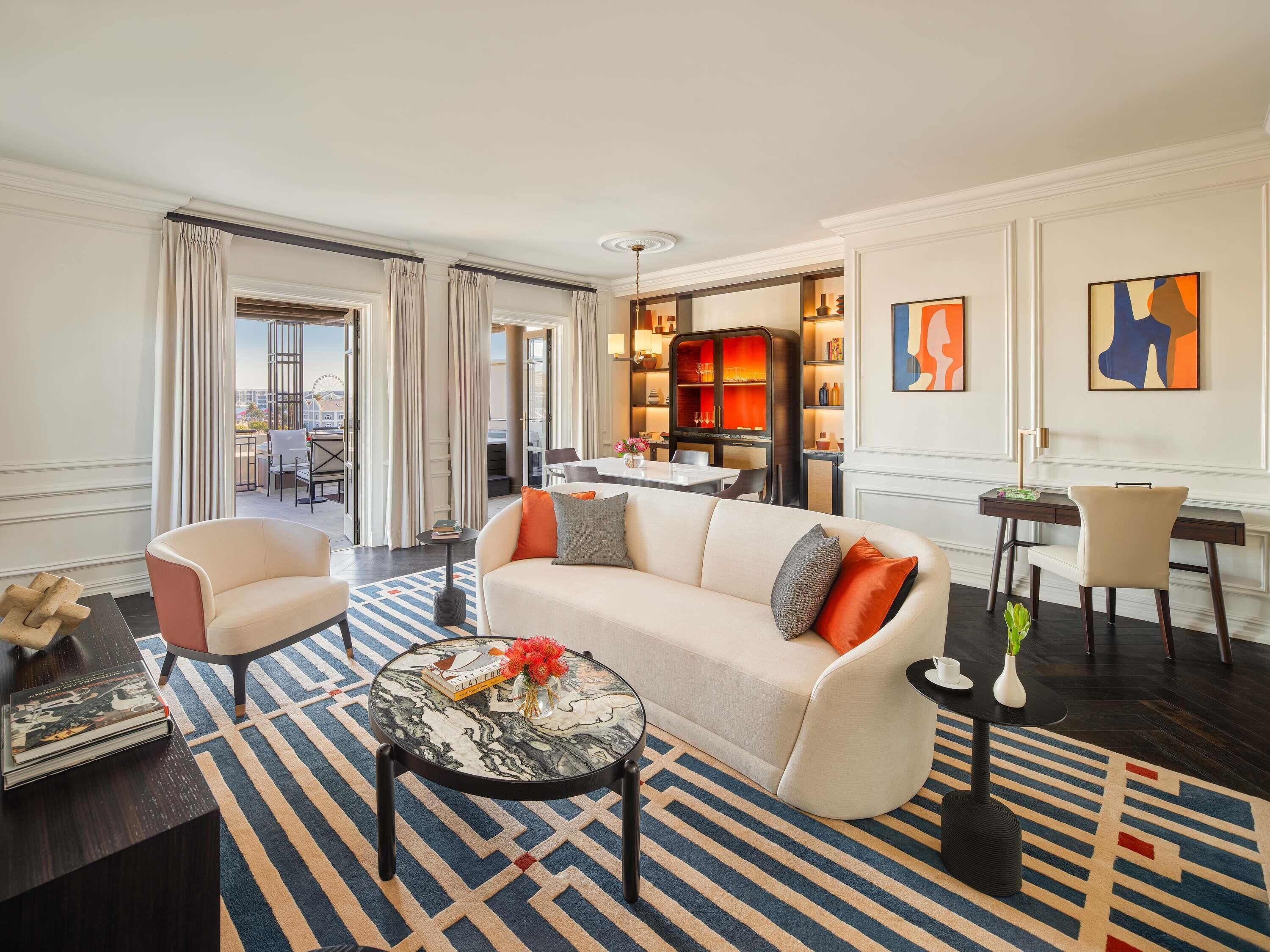 Una habitación de hotel moderna con sofá, sillones, zona de comedor y obras de arte en las paredes.