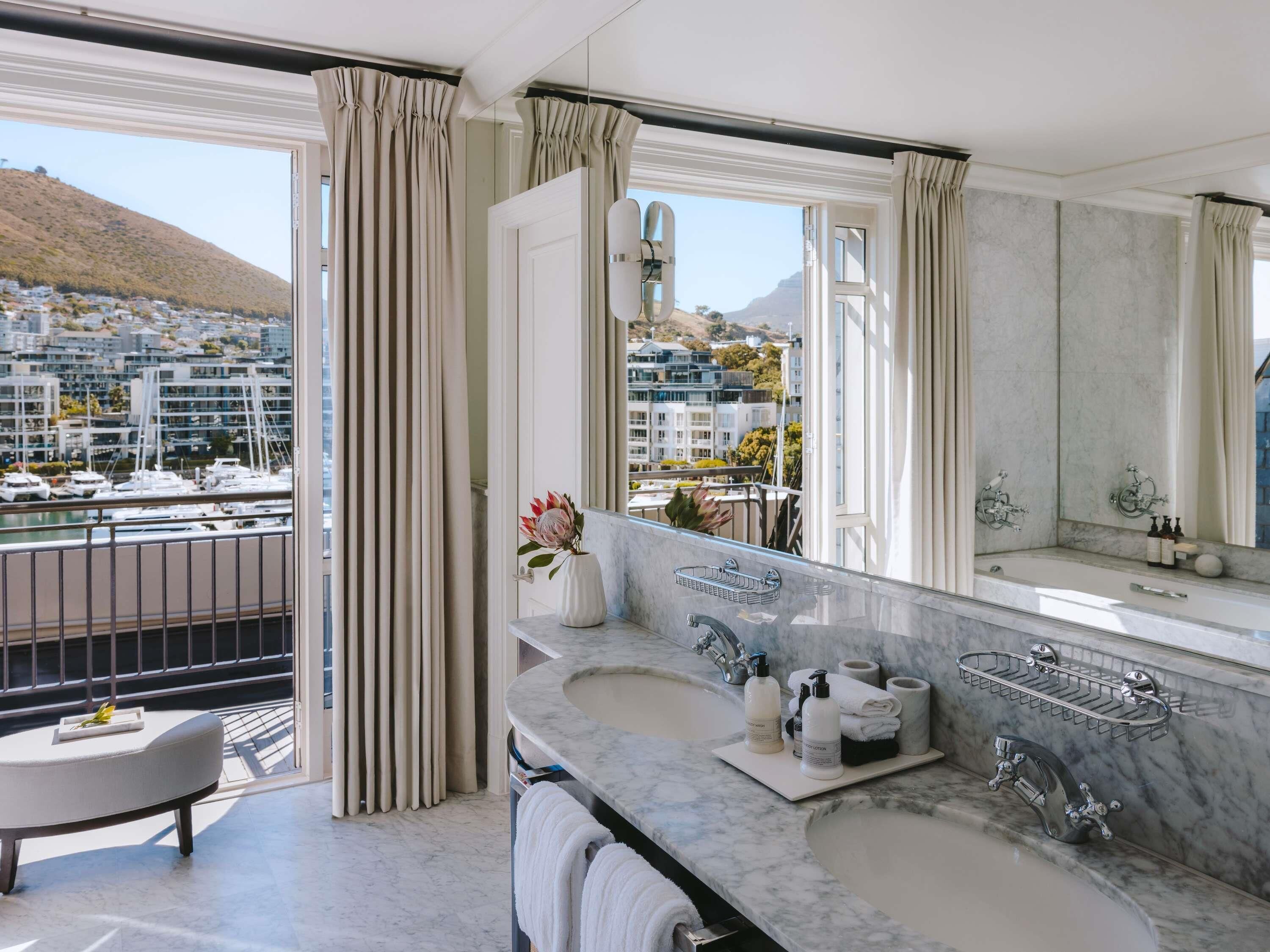 A modern bathroom with a large window, a marble sink, and a view of a marina and buildings.