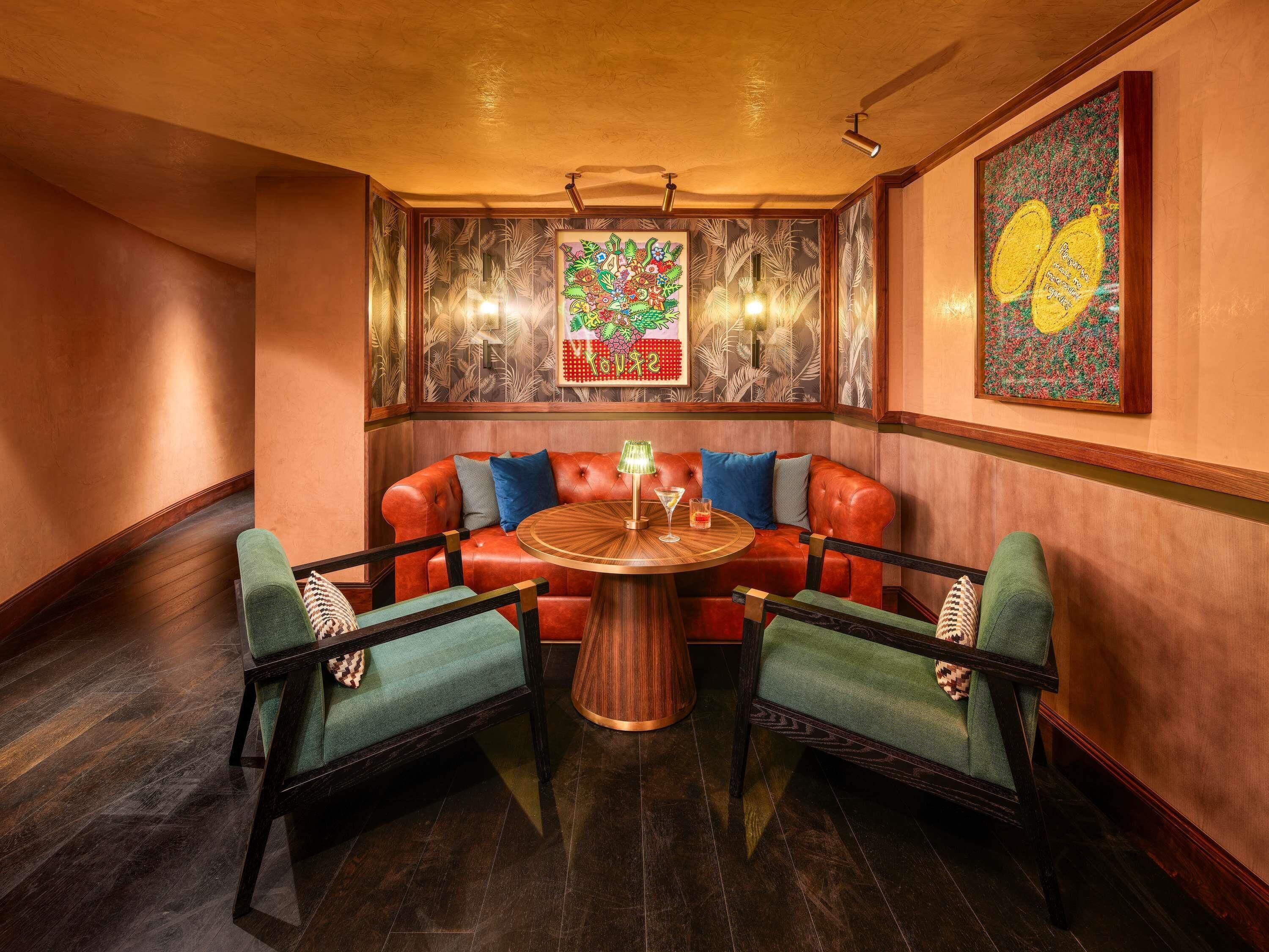 Een gezellig hoekje met een rode leren bank, twee groene fauteuils en een houten salontafel.