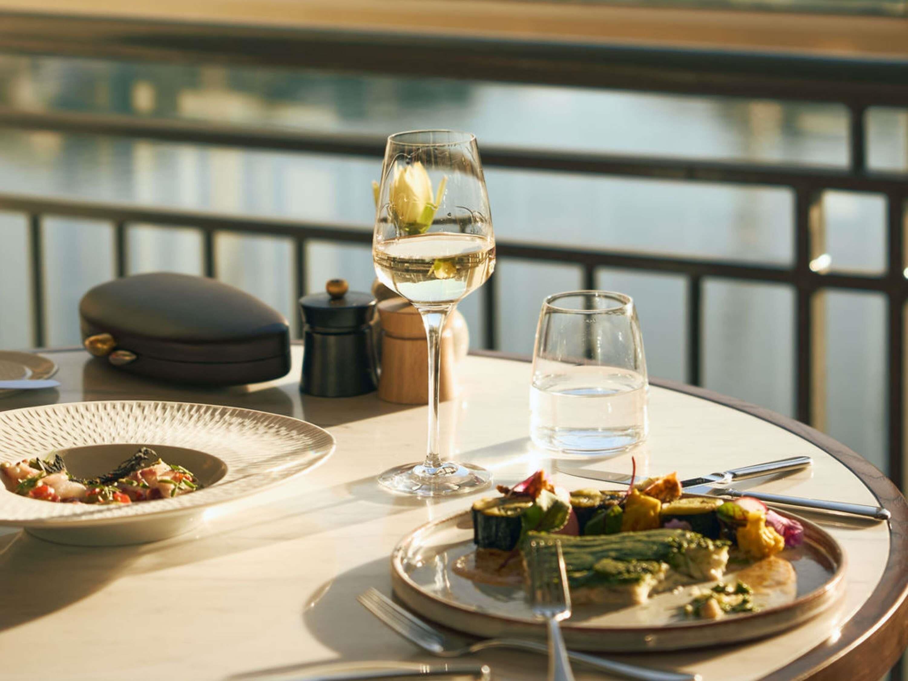 A dining table with plates of food, a wine glass, and a water glass.