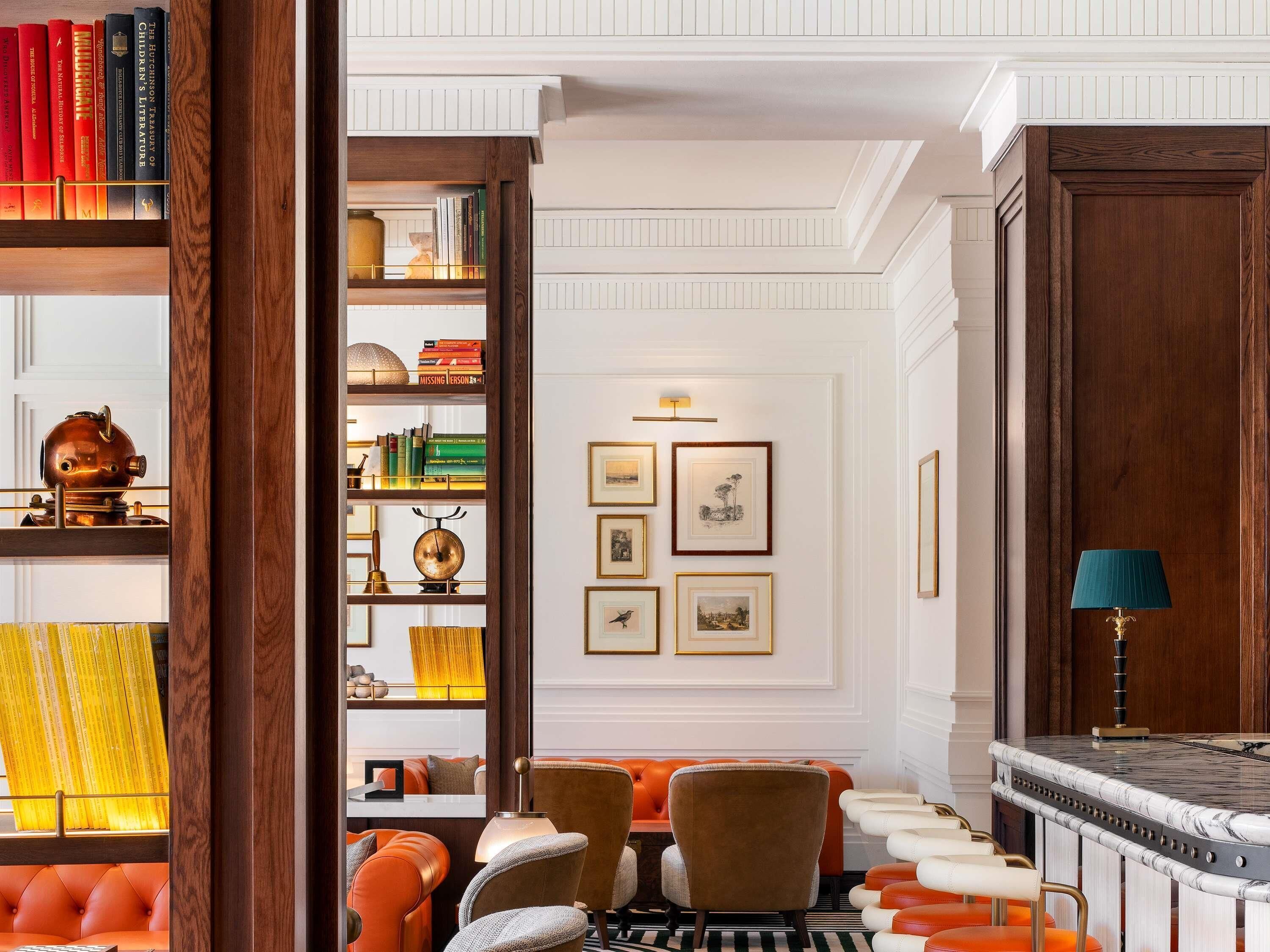 Une bibliothèque avec des étagères, une cheminée, des tableaux encadrés et un coin salon avec des fauteuils et des poufs.