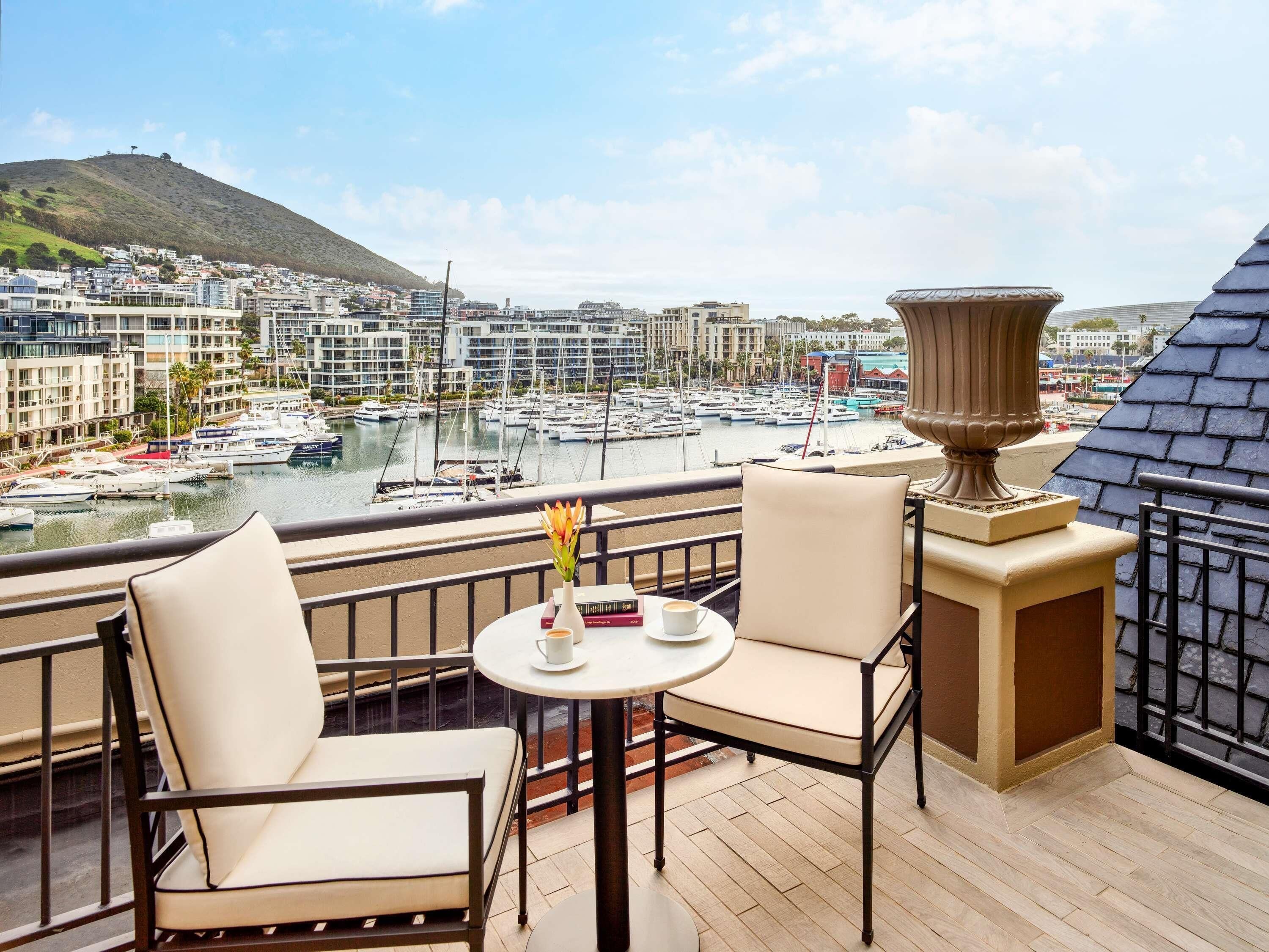 Un balcon avec deux chaises et une table, donnant sur une marina où l’on peut admirer des bateaux et des bâtiments.