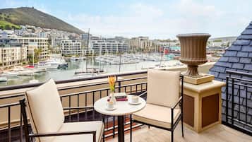 A balcony with two chairs and a table, overlooking a marina with boats and buildings.