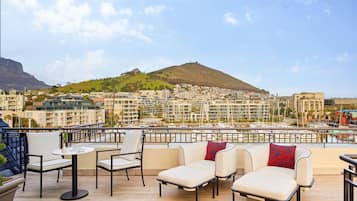 A rooftop terrace with outdoor seating, a view of a cityscape, and a hill in the background.
