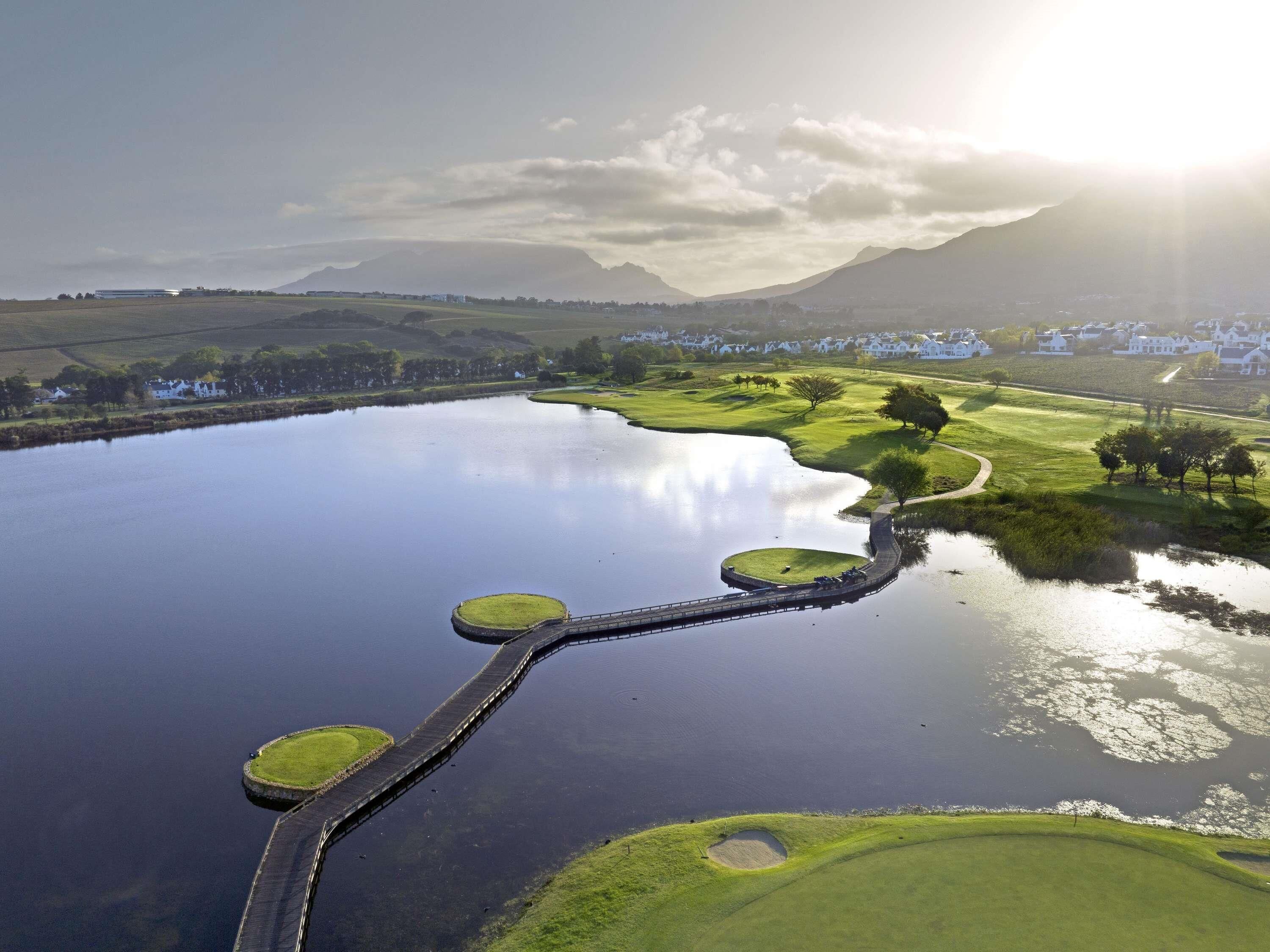 A golf course with a water body, a bridge, and a mountainous backdrop.