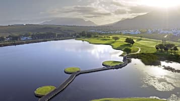A golf course with a water body, a bridge, and a mountainous backdrop.