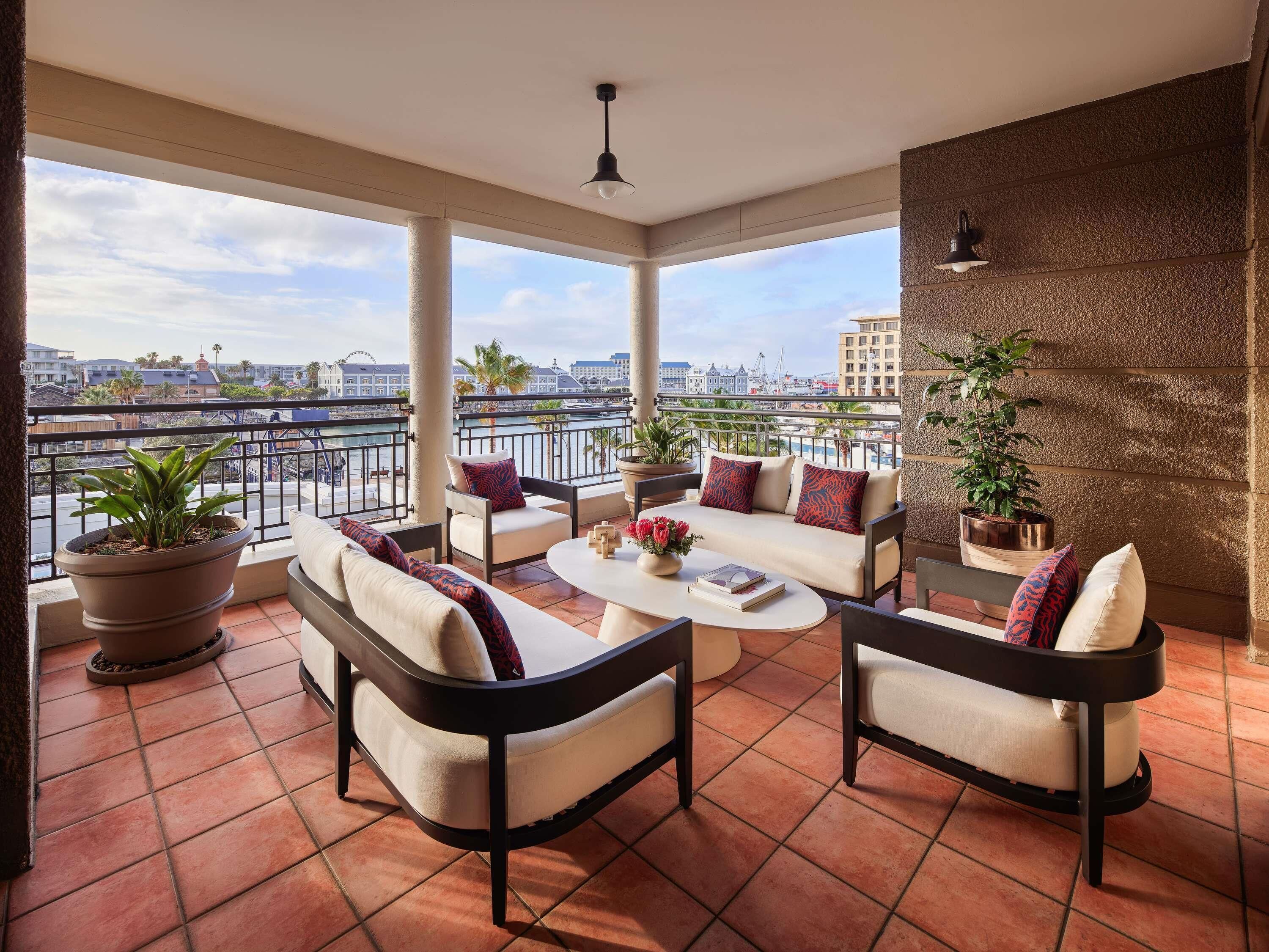 A balcony with a sofa, chairs, a coffee table, and potted plants.