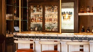 Zona de bar con mostrador de mármol, tres taburetes de cuero, una vitrina con botellas y un candelabro.