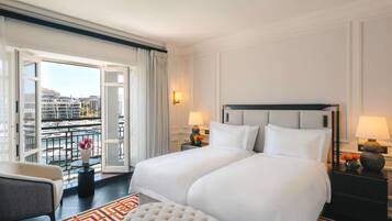 A hotel room with a large bed, two bedside tables, a chair, a view of the city through a balcony, and a patterned rug.