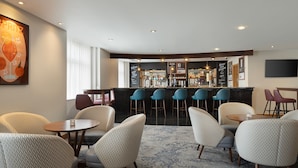 A bar area with a counter, stools, and a seating area with round tables and chairs. - Delta Hotels Bexleyheath (Bexleyheath)