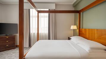 Une chambre d’hôtel avec un lit à baldaquin, un téléviseur à écran plat, une table de chevet en bois et une lampe.