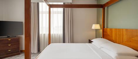 Habitación de hotel con cama con dosel, televisor de pantalla plana, mesita de noche de madera y lámpara.