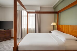 Habitación de hotel con cama con dosel, televisor de pantalla plana, mesita de noche de madera y lámpara.