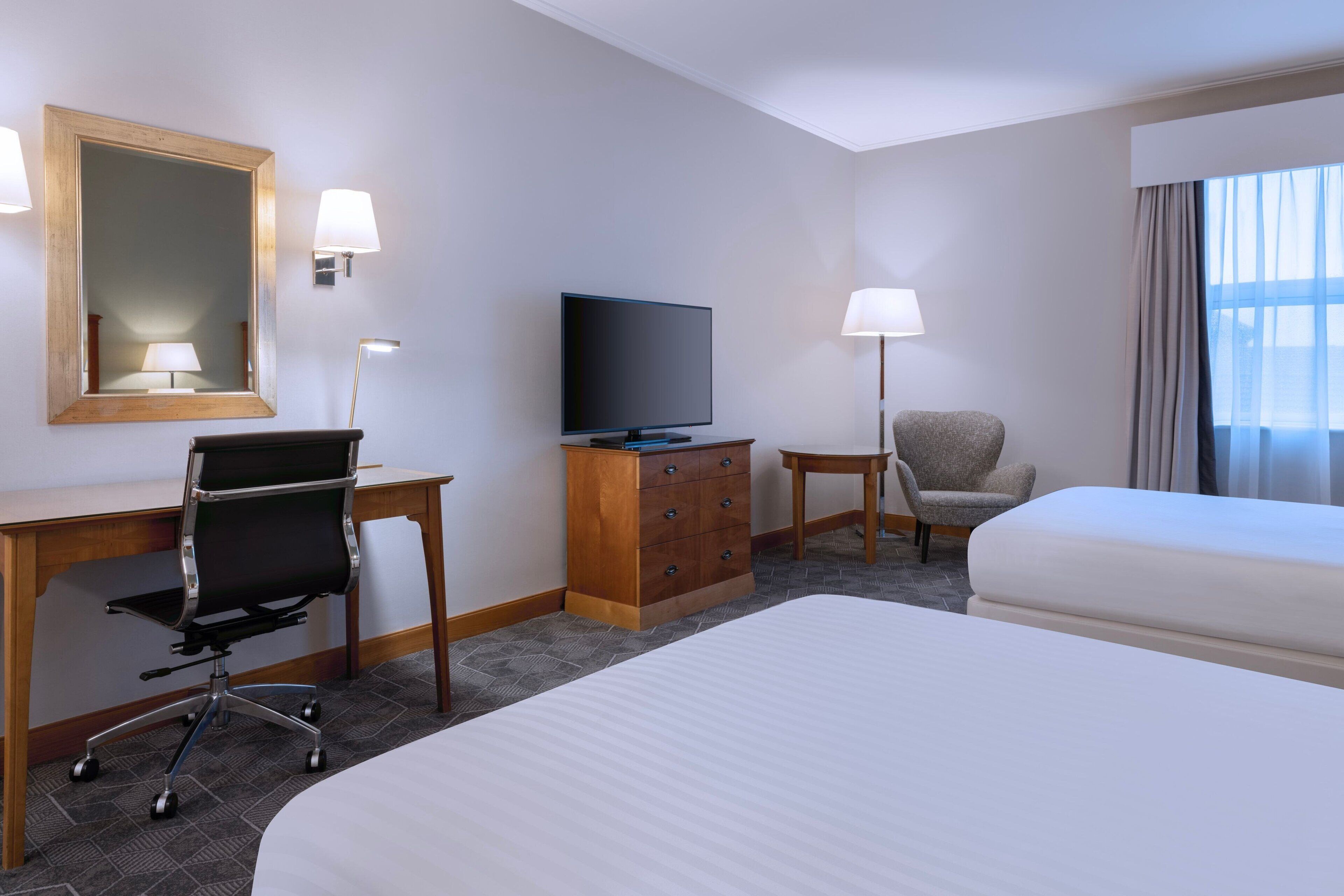 A hotel room with a bed, a desk with a computer, a television, a chair, and a dresser.