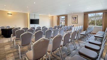 A conference room with rows of chairs, a table with water bottles, a TV, and a window with a view.