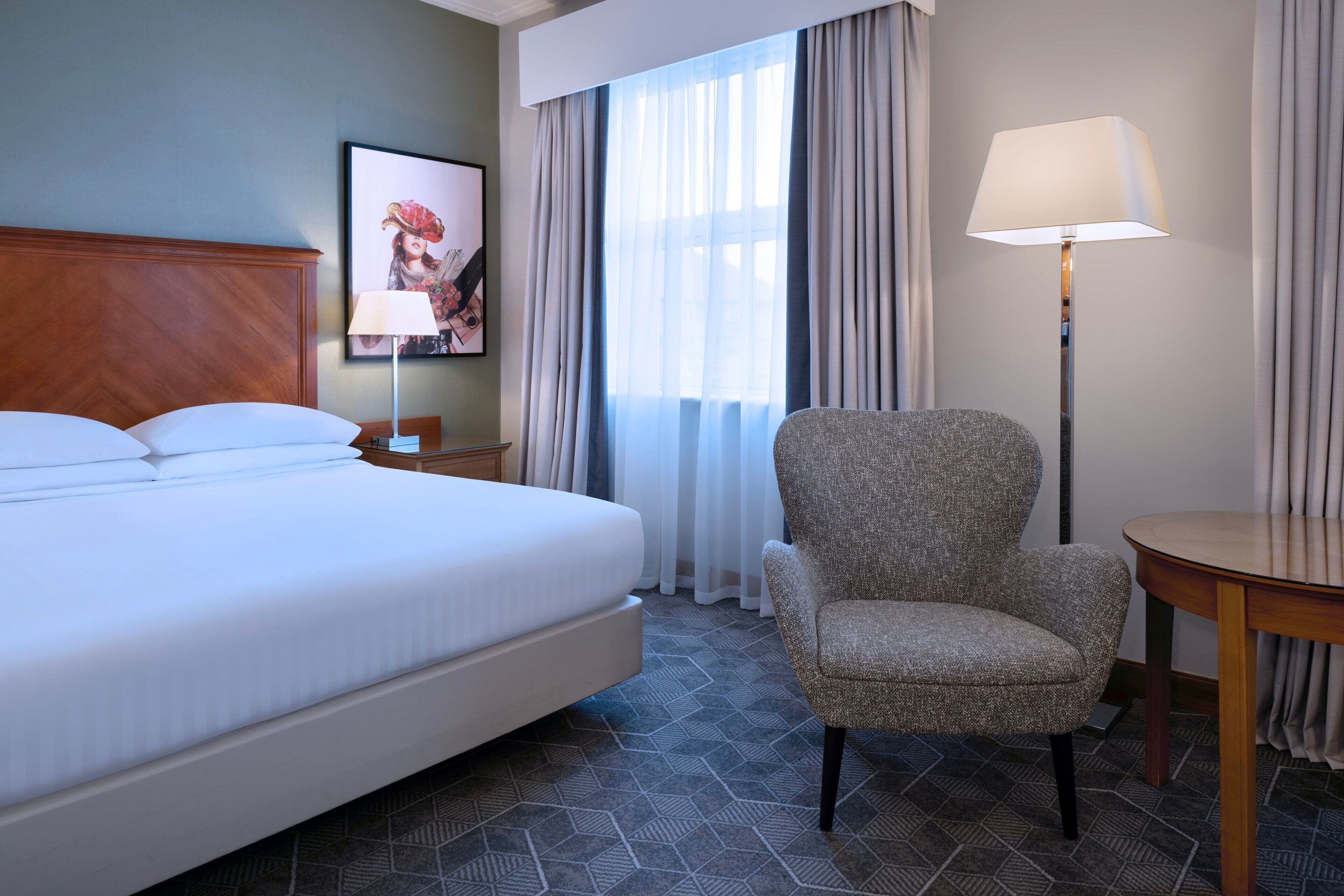 A hotel room with a large bed, a chair, a table, and a lamp.
