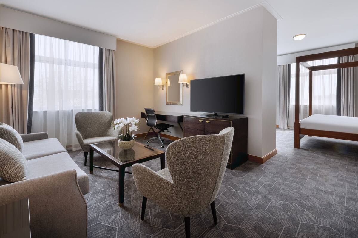 A hotel room with a sofa, armchair, desk, TV, and a bed.