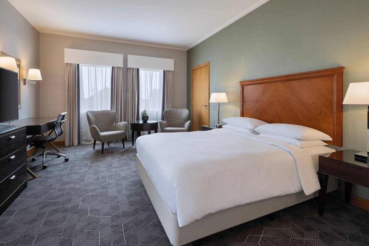 A hotel room with a large bed, two armchairs, a desk, and a television.