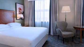 Habitació d'hotel amb un llit gran, una cadira, un escriptori i una làmpada.