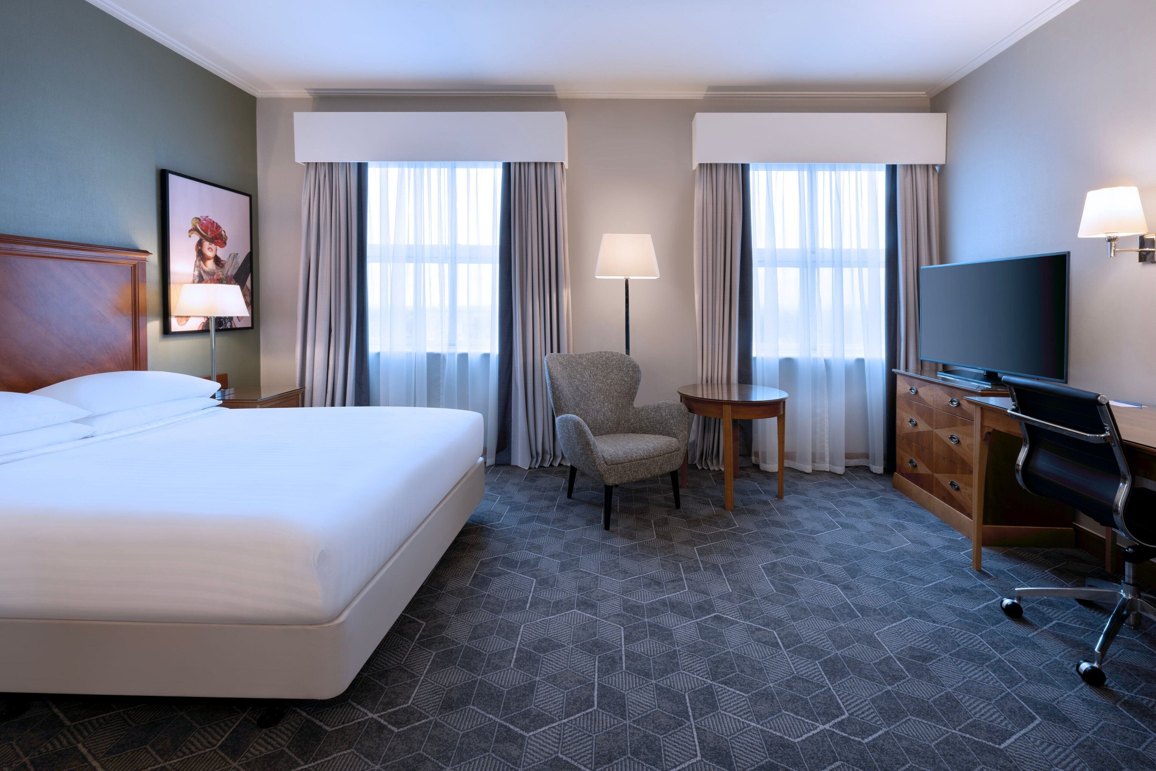 Ein Hotelzimmer mit einem großen Bett, einem Schreibtisch mit Stuhl, einem Fernseher und einem kleinen Tisch.