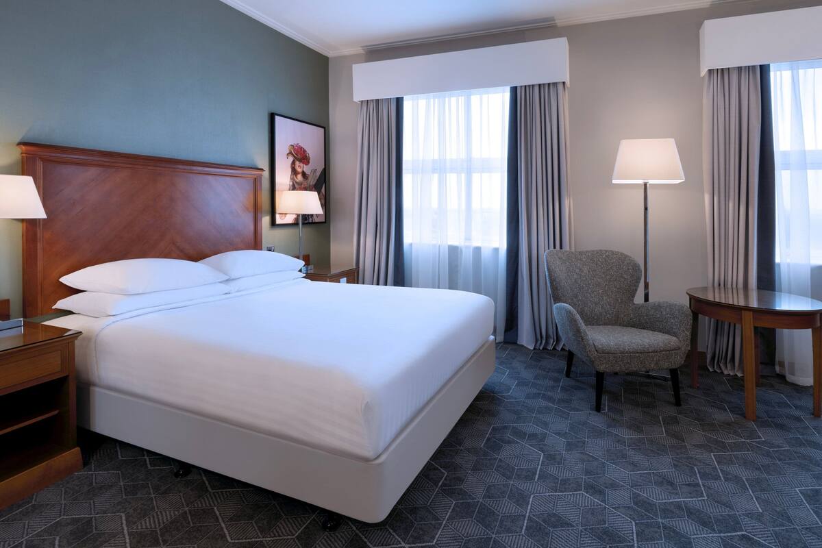 A hotel room with a large bed, a chair, a table, and a lamp.