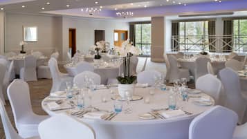 A banquet hall with round tables set for dining, white chairs, and a chandelier.